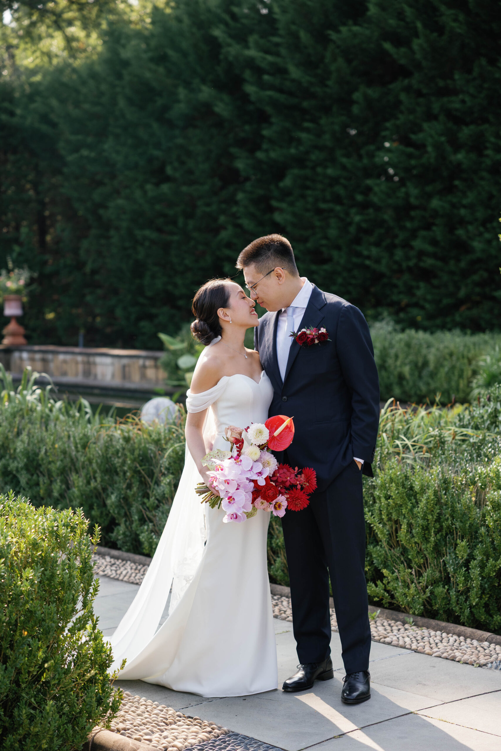 A Chinese couple in wedding attire with gorgeous red, pink, and purple flowers at a botanical garden in new york